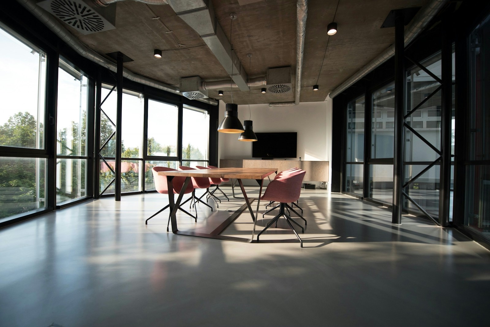 Sala de reuniones con ventanales amplios y luz natural de mañana proyectando sombras en el suelo.