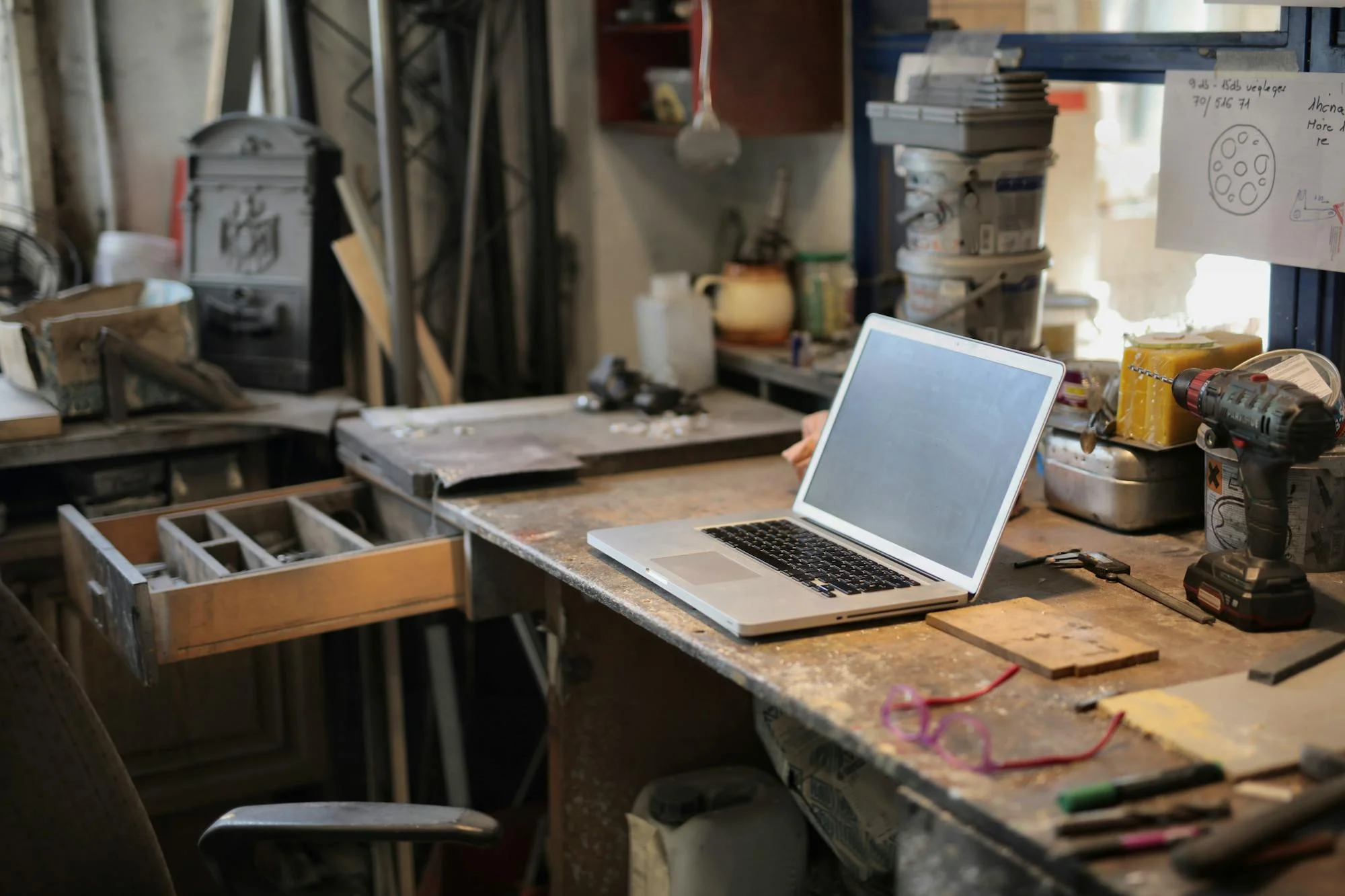Laptop abierto sobre mesa de un taller con herramientas alrededor.